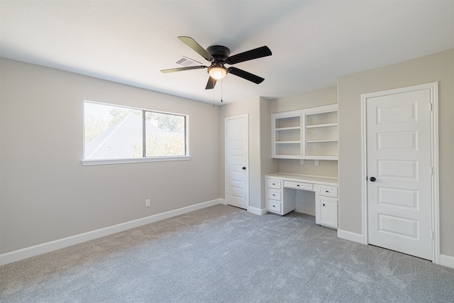 unfurnished bedroom with light carpet, built in desk, and ceiling fan