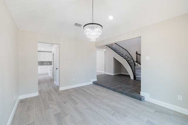 unfurnished living room with lofted ceiling, light hardwood / wood-style flooring, and an inviting chandelier