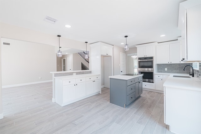 kitchen featuring a kitchen island, stainless steel double oven, sink, pendant lighting, and white cabinetry