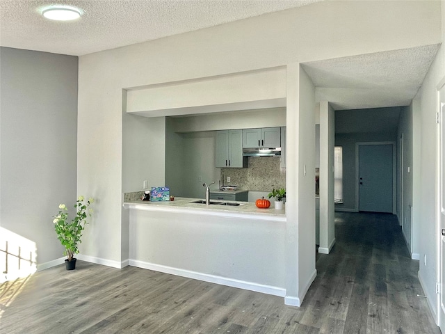 kitchen featuring kitchen peninsula, tasteful backsplash, a textured ceiling, dark wood-type flooring, and sink