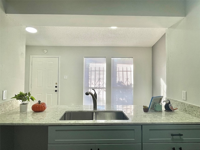 kitchen with light stone countertops, a textured ceiling, gray cabinets, and sink