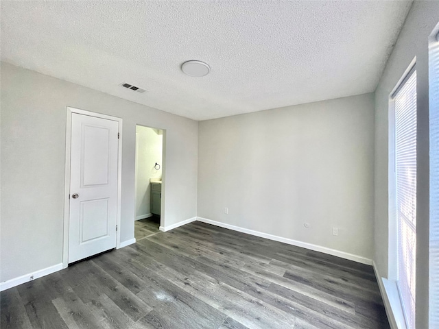 unfurnished bedroom with a textured ceiling, dark hardwood / wood-style floors, and ensuite bathroom