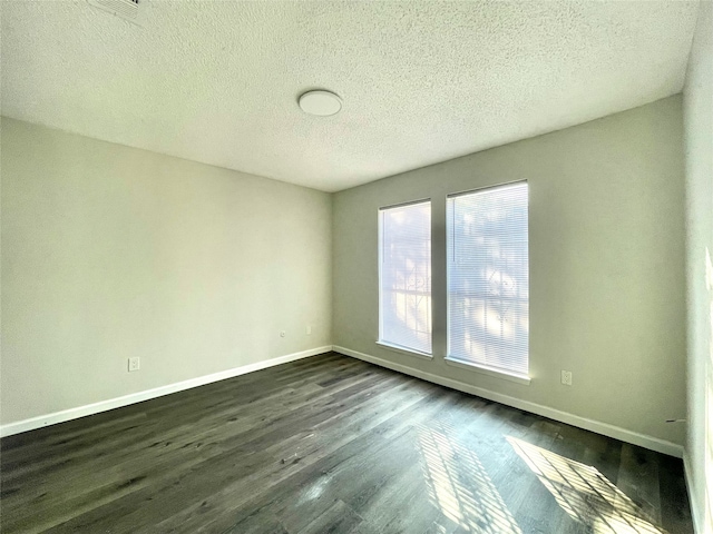 empty room with a textured ceiling, dark hardwood / wood-style floors, and plenty of natural light