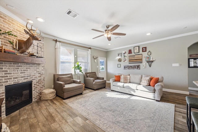 living room featuring ceiling fan, wood-type flooring, crown molding, and a brick fireplace