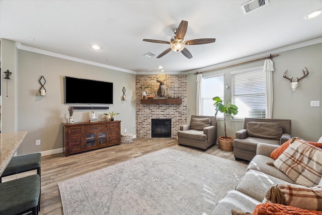 living room featuring a brick fireplace, ceiling fan, crown molding, and light hardwood / wood-style flooring