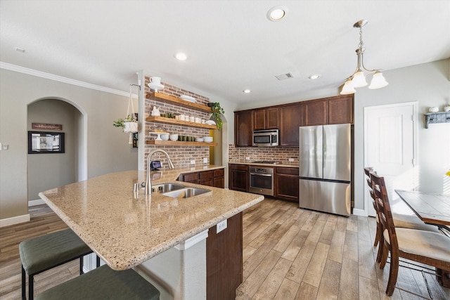 kitchen with appliances with stainless steel finishes, light wood-type flooring, light stone counters, crown molding, and sink