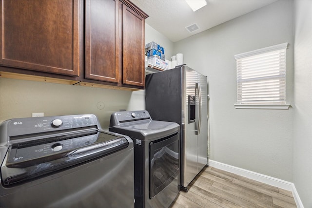 laundry area featuring cabinets, washing machine and dryer, and light hardwood / wood-style flooring