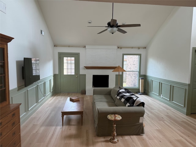 living room featuring light hardwood / wood-style floors, high vaulted ceiling, a large fireplace, and ceiling fan