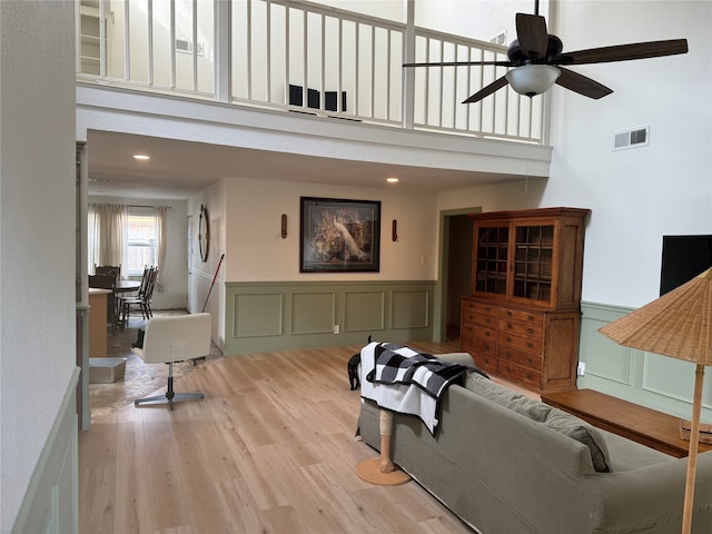 living room with a high ceiling, light wood-type flooring, and ceiling fan