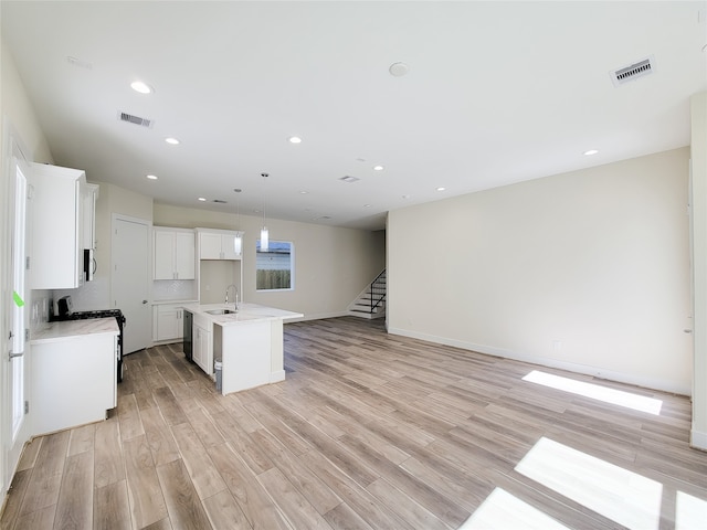 kitchen with white gas range oven, light hardwood / wood-style flooring, a center island with sink, and white cabinets