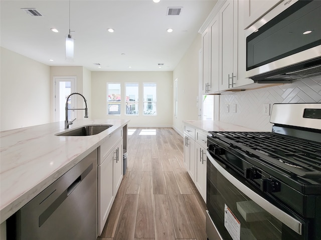 kitchen with appliances with stainless steel finishes, sink, pendant lighting, white cabinets, and light hardwood / wood-style flooring