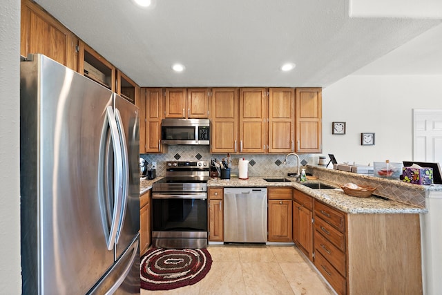 kitchen featuring decorative backsplash, kitchen peninsula, sink, appliances with stainless steel finishes, and light stone counters