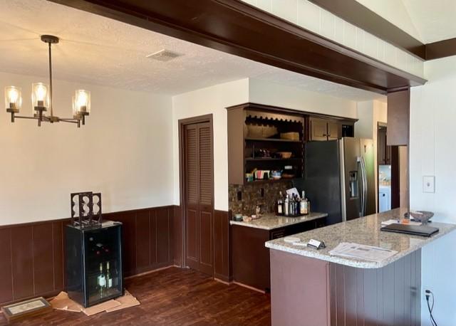 bar with a chandelier, a wainscoted wall, visible vents, stainless steel refrigerator with ice dispenser, and dark wood-style floors