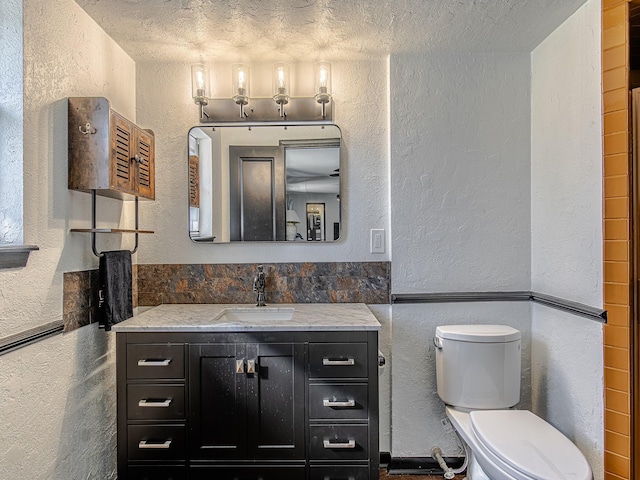 bathroom featuring a textured ceiling, a textured wall, vanity, and toilet