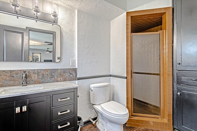 full bath with a textured wall, vanity, a shower stall, and toilet