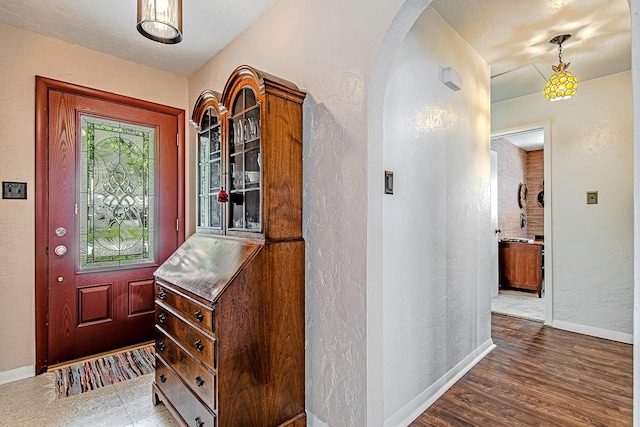 foyer featuring arched walkways, a textured wall, wood finished floors, and baseboards