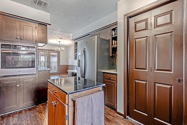 kitchen with dark wood-style floors, stainless steel appliances, visible vents, brown cabinetry, and a textured ceiling