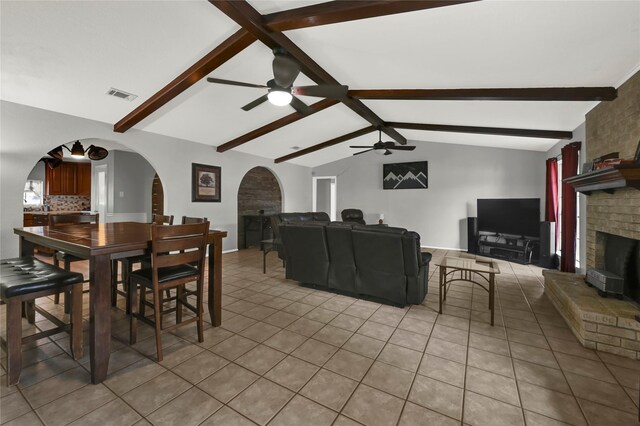 tiled dining area featuring a fireplace, lofted ceiling with beams, and ceiling fan