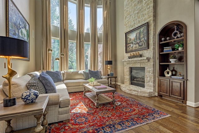 living room featuring dark wood-type flooring, a fireplace, a towering ceiling, and built in features