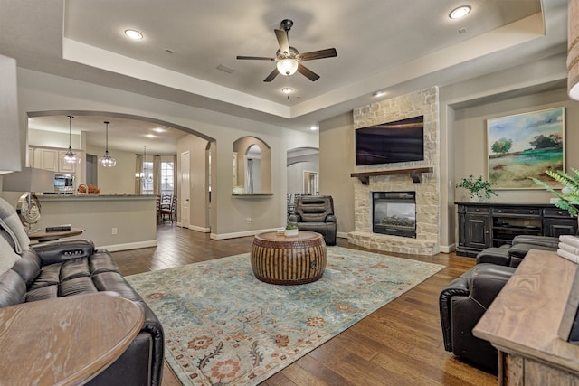 living room with dark hardwood / wood-style floors, a tray ceiling, a fireplace, and ceiling fan