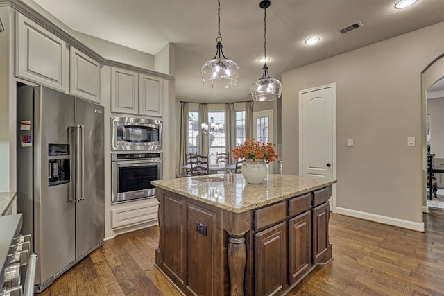 kitchen featuring dark wood-type flooring, light stone countertops, appliances with stainless steel finishes, and dark brown cabinetry