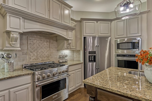 kitchen with light stone countertops, high quality appliances, dark hardwood / wood-style flooring, pendant lighting, and decorative backsplash