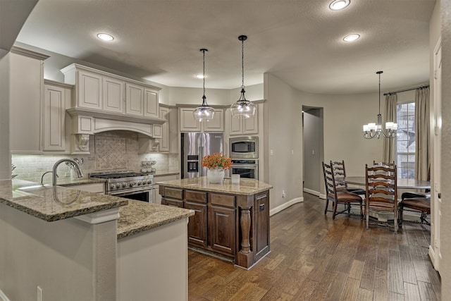 kitchen with dark wood-type flooring, a center island, decorative light fixtures, appliances with stainless steel finishes, and light stone counters