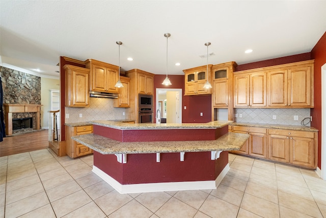 kitchen with tasteful backsplash, appliances with stainless steel finishes, a fireplace, hanging light fixtures, and a kitchen island with sink