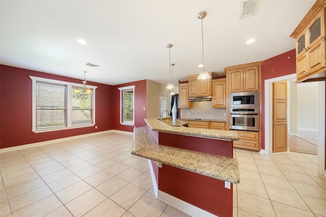 kitchen with light stone countertops, pendant lighting, backsplash, and an island with sink