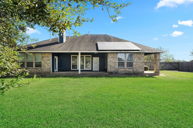 rear view of property with solar panels and a lawn