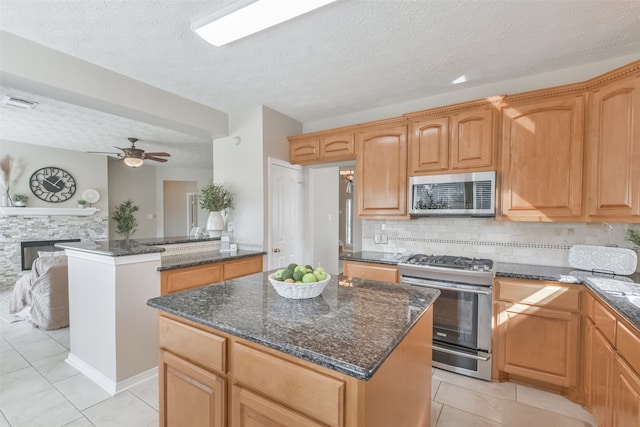 kitchen with a kitchen island, a stone fireplace, light tile patterned floors, and stainless steel appliances