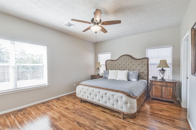 bedroom with a textured ceiling, multiple windows, ceiling fan, and dark hardwood / wood-style floors