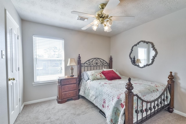 bedroom with ceiling fan, light colored carpet, a textured ceiling, and multiple windows