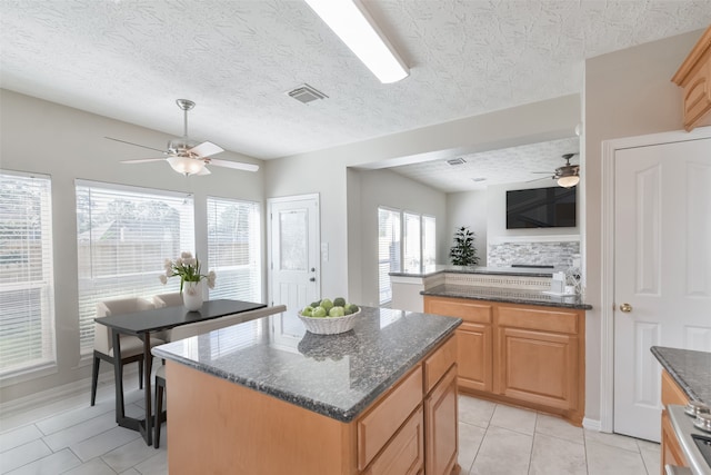 kitchen with a center island, lofted ceiling, dark stone countertops, light tile patterned floors, and a textured ceiling