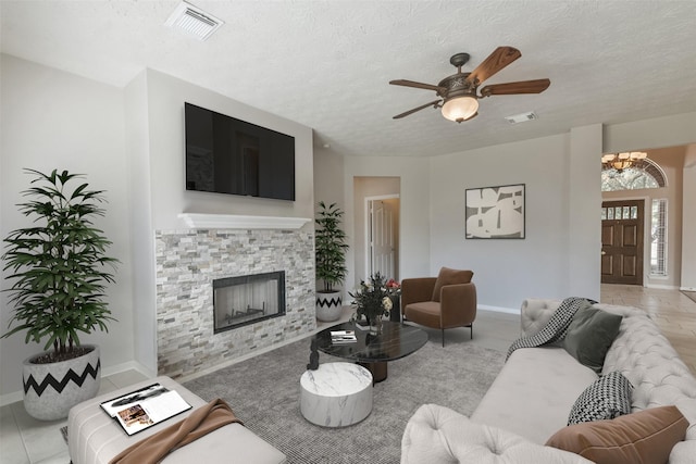 tiled living room with ceiling fan, a stone fireplace, and a textured ceiling