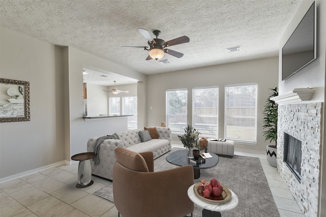 living room featuring a textured ceiling, ceiling fan, light tile patterned flooring, and a fireplace