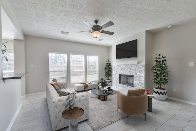 living room with a fireplace, light tile patterned floors, a textured ceiling, and ceiling fan