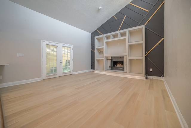 unfurnished living room with french doors, hardwood / wood-style flooring, built in features, a textured ceiling, and high vaulted ceiling