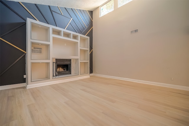 unfurnished living room featuring a high end fireplace, a high ceiling, a textured ceiling, and wood-type flooring