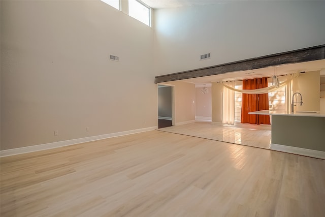 unfurnished living room with a healthy amount of sunlight, a high ceiling, and light hardwood / wood-style floors