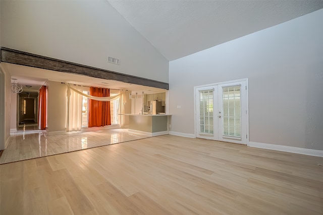 unfurnished living room featuring french doors, high vaulted ceiling, and light wood-type flooring