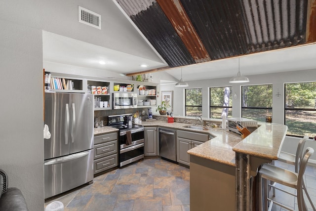 kitchen with a breakfast bar area, kitchen peninsula, gray cabinetry, stainless steel appliances, and light stone counters