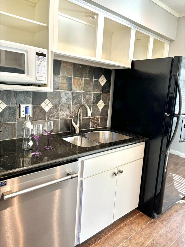 kitchen with stainless steel dishwasher, ornamental molding, dark stone counters, sink, and white cabinets