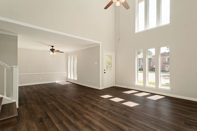 unfurnished living room with dark wood-type flooring, ceiling fan, a towering ceiling, and ornamental molding