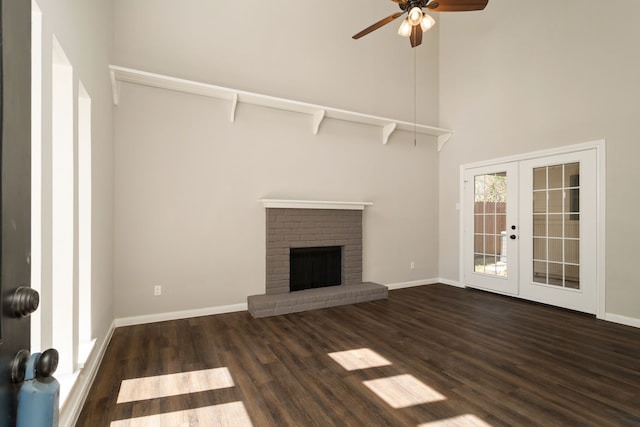 unfurnished living room with a fireplace, french doors, ceiling fan, a high ceiling, and dark hardwood / wood-style floors