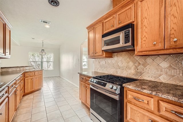 kitchen featuring tasteful backsplash, appliances with stainless steel finishes, pendant lighting, dark stone countertops, and light tile patterned floors