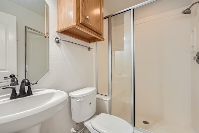 bathroom featuring toilet, a shower with shower door, and sink