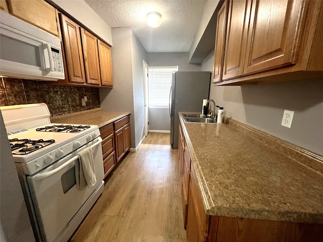 kitchen with a textured ceiling, sink, light wood-type flooring, and white appliances