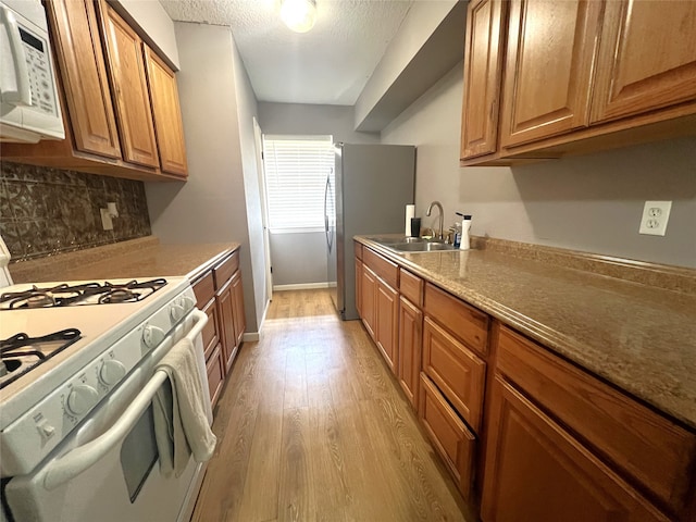 kitchen featuring white appliances, sink, a textured ceiling, light hardwood / wood-style floors, and decorative backsplash