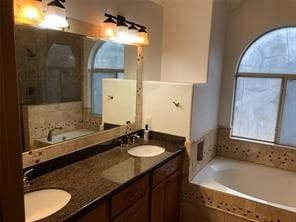 bathroom featuring vanity, a relaxing tiled tub, and plenty of natural light